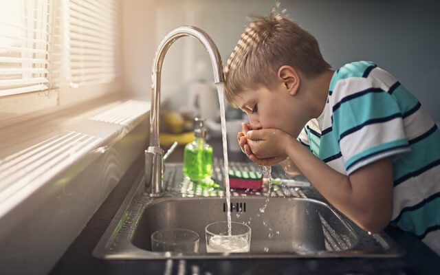 Little boy drinking tap water from sink faucet.